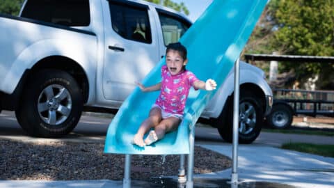 An excited small girl slides down a pool slide into a pool