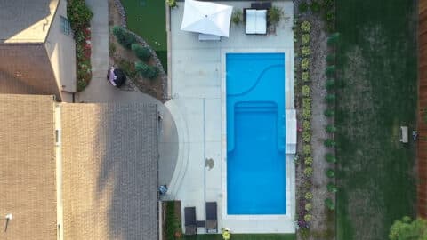 An aerial shot of a pool in a backyard- it is rectangle in shape