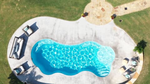 An aerial shot of a pool in a backyard- it has a round, long shape